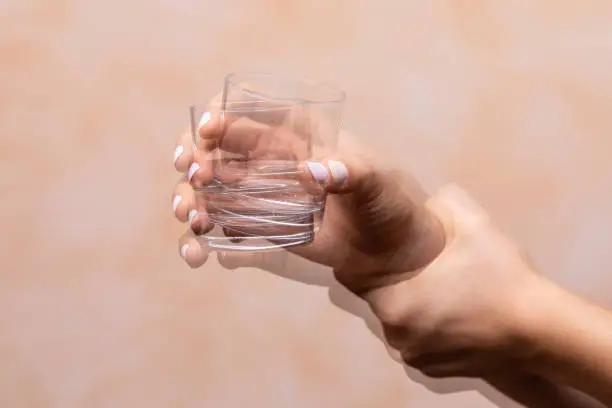 Photo of hand holding drinking glass suffering from Parkinson's disease