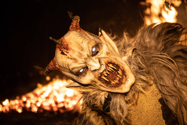 Man masked with a spooky Krampus character costume and fire in the background  holidays concept Tarvisi, Italy – December 05, 2018: A Man masked with a spooky Krampus character costume and fire in the background  holidays concept demon stock pictures, royalty-free photos & images
