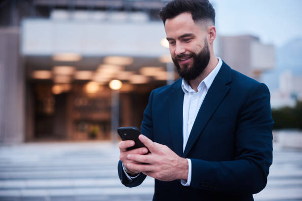 istock Smiling businessman reading a phone text outside his building after work 1436693644