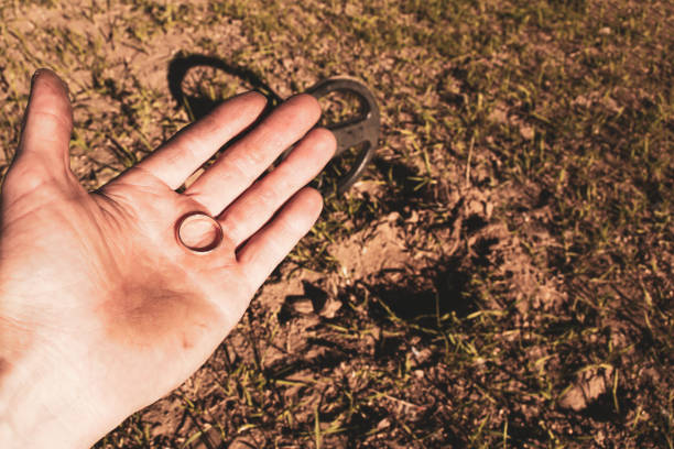 un antico anello d'oro in mano a un cercatore, trovato su un vecchio tratto con l'aiuto di un metal detector, il primo piano e lo sfondo sono sfocati con un effetto bokeh - searcher foto e immagini stock