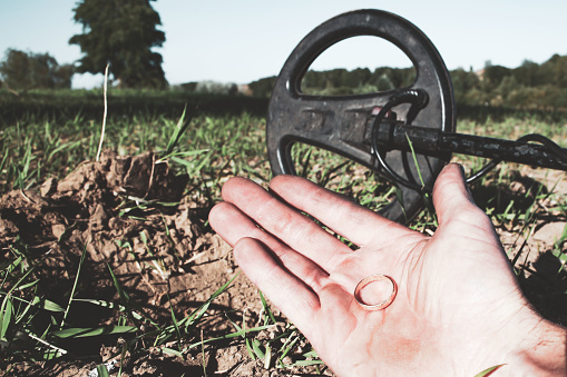 an antique gold ring in the hand of a searcher, found on an old tract with the help of a metal detector, the foreground and background are blurred with a bokeh effect