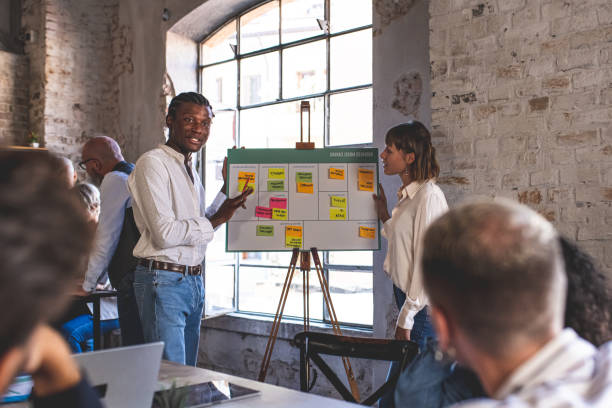 istock Mixed age range business people working in office, creatives and designers working on new project, startup concept, young African American man explainign strategy. 1436694925