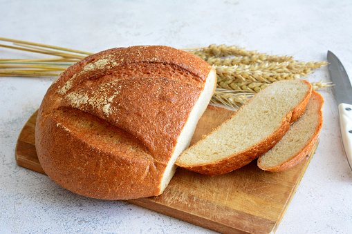 fresh wheat bread with slices and knife on cutting board isolated, close-up