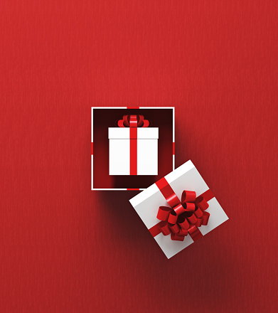 White gift box is sitting inside of another gift box on red background. Vertical composition with copy space, Great use for sale concepts.