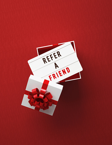 Refer a friend written lightbox sitting over white gift box on red background. Vertical composition with copy space, Great use for refer a friend concepts.