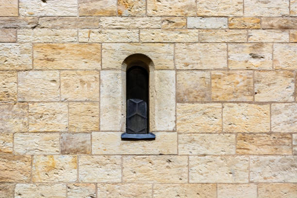 Narrow window, closed with iron shutters, in a stone wall of red and beige blocks. From the Window of the World series.