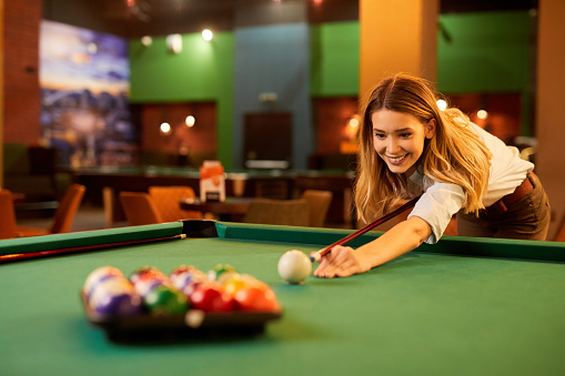Young woman aiming and playing pool in the pool hall