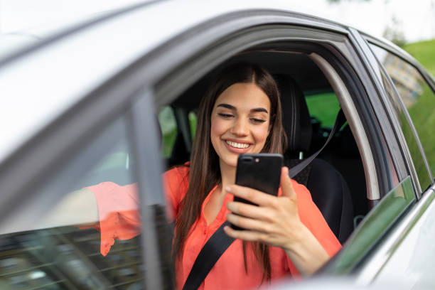 a jovem usa um celular no carro. isolamento de celular tecnológico. internet e mídias sociais. mulher com smartphone no carro. garota está usando um smartphone - driving mobile phone car talking - fotografias e filmes do acervo