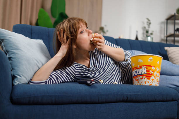 istock Young woman is focused on watching a movie, eating popcorn while lying on the sofa 1436710587