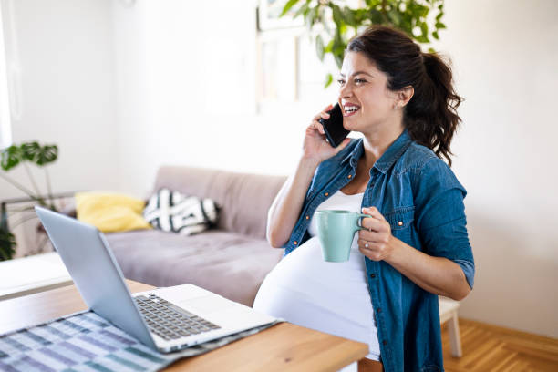 Pregnant woman sitting working on laptop drinking coffee and using phone stock photo