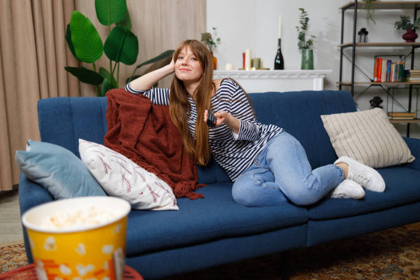 istock Young woman watching tv and using remote control on sofa at home 1436712600