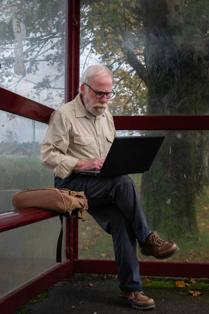 пенсионер сидит на автобусной остановке с ноутбуком - dumfries and galloway стоковые фото и изображения