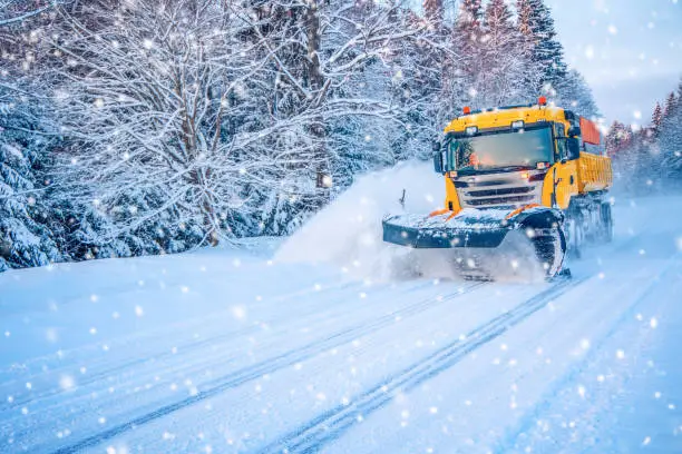 Snow plow truck cleaning road in snowstorm. Snowfall on the driveway.