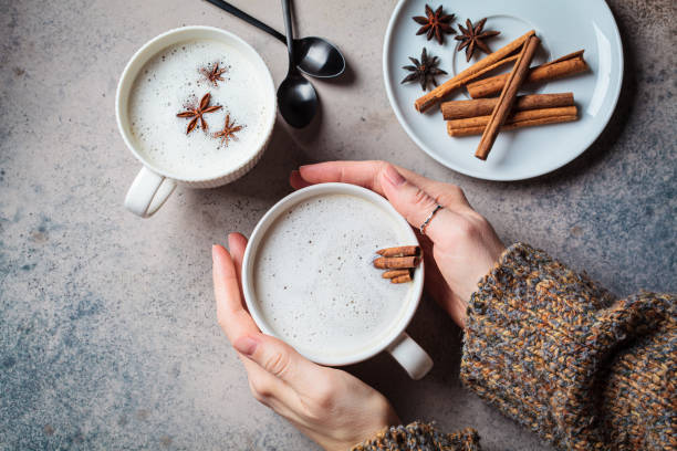 Homemade chai latte with cinnamon and star anise in white cup, dark background. Homemade chai latte with cinnamon and star anise in white cup in hands, dark background, top view. chai stock pictures, royalty-free photos & images