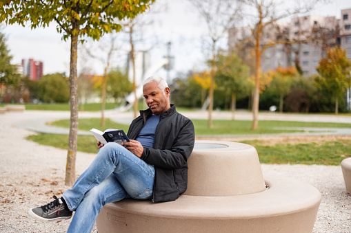 Happy Retired Senior Man Reading A Book In The Park