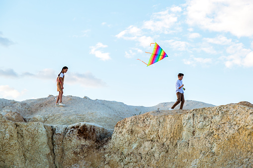 Teenagers run through mountains with kite flying summer vacation concept.