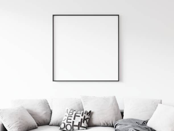 istock Square picture frame with thin black border hanging on white wall above pillows laying on sofa in living room. 3D illustration. 1436728074