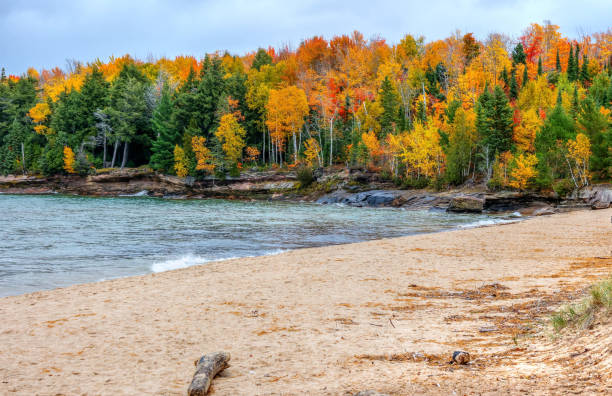Blond woman walks alone along the shoreline covered in Rhyolite rocks at Iona Beach, also called Singing Beach for the tinkling sound heard when waves wash over the red rocks, Lake Superior, North Shore,  Two Harbors, Minnesota