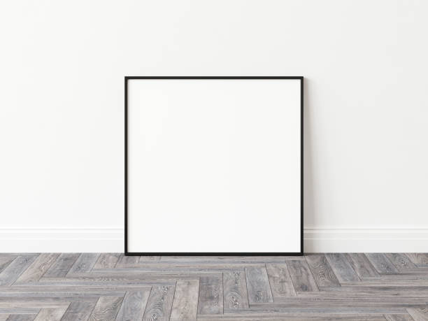 istock Blank square picture frame with thin black border standing on wooden parquet floor leaning on white wall. 3D Illustration. 1436728255