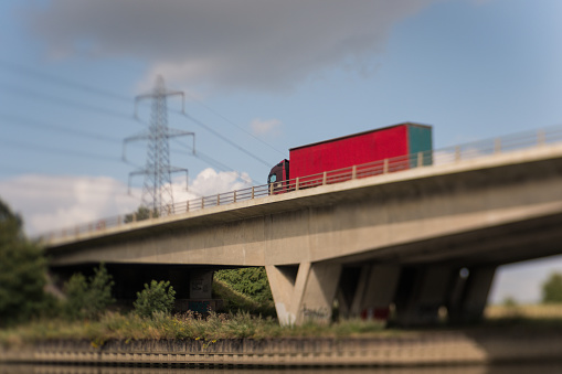 freight transportation articulated lorry driving over a motorway river bridge with an industrial backround of power station and electrical lines. Taken with a Lensbaby for intentional blur