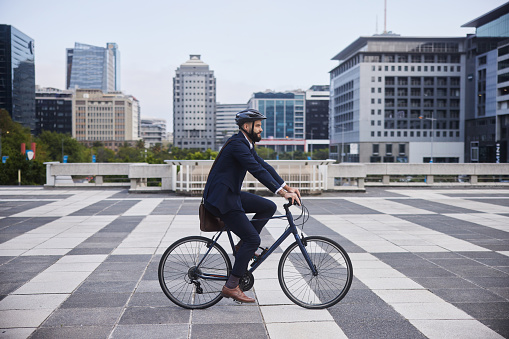 Young businessman wearing a cycling helmet and carrying a bag smiling while leaving work for the day on his bicycle