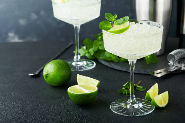 istock Margarita cocktail with lime, tequila, mint and ice on dark table with amazing backlight, copy space. Classic Margarita or Daiquiry Cocktail. Bar card or counter concept. Selective or soft focus. 1436735544