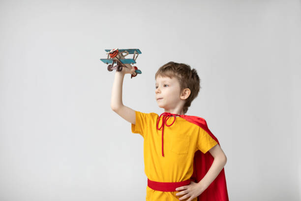 istock Dreamy boy in a red cape plays with an airplane toy. 1436741694