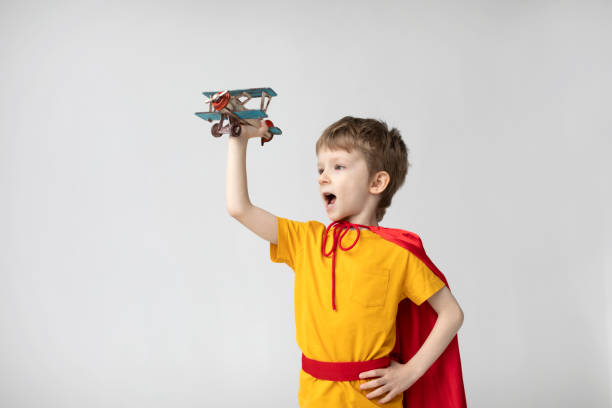 istock Dreamy boy in a red cape plays with an airplane toy. 1436743243