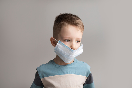5-7 years old child wearing surgical mask. Little boy trying to stay healthy by wearing a mask to protect. Boy wearing anti virus mask staying at home
