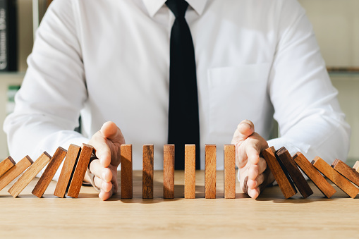 Risk management, business man hand Stop the continuous falling of wooden dominoes, stop the impact of the business crisis. hedging Solving business problems for success.