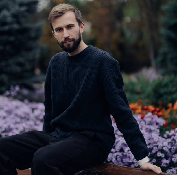 istock Young happy man rests on bench in park near flowerbed. 1436744009