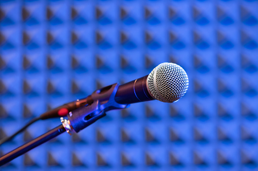 Soft focus of professional microphone mounted on stand against blue soundproof wall in recording studio