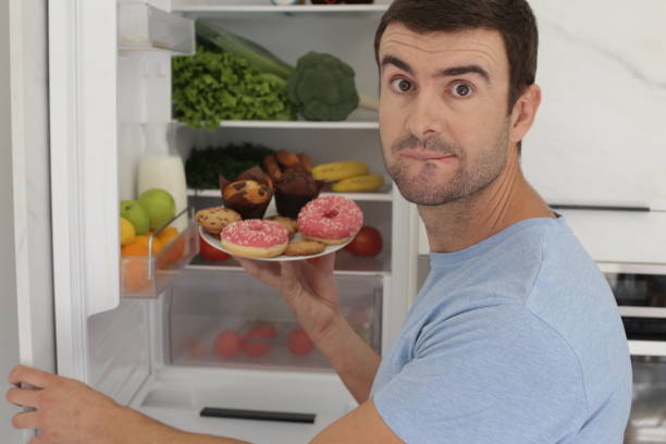 man choosing junk food over vegetables - cake pick imagens e fotografias de stock