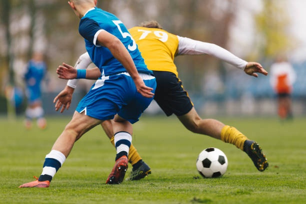 fußballspieler treten in einem turnierspiel in einem duell gegeneinander an. fußballspiel am sonnigen sommertag. adul fußballspieler im blauen und gelben trikot laufen klassischen fußball auf rasenplatz - kick er stock-fotos und bilder