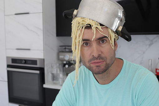 A chaotic chef is trying to make some pasta. He made a mistake and the past fell all over his head. This is a comedic image.
