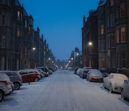 Cars parked on a snow covered residential street in Edinburgh's Bruntsfield district at dusk.