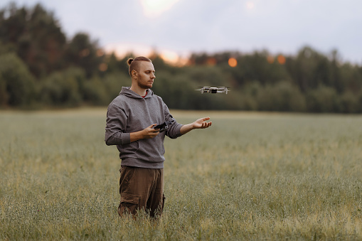 Man controlling a drone with a remote control stands in a field. Drone operator. Aerial photography. Recording footage in the air. New technologies and trends in photo and video shooting.