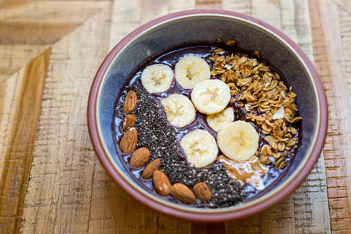 Acai bowl made with açai, coconut milk, sliced bananas, chia seeds, granola, almonds and peanut butter in a bowl on a table