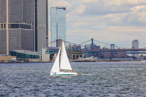 New York, Manhattan, USA. 10.27.2022. Gorgeous view of white sailboat with tourists on Manhattan buildings background.