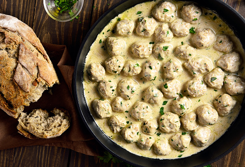 Diet swedish meatballs with creamy white sauce in cooking pan over wooden background. Top view, lat lay, close up