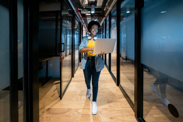 Happy IT technician working at the office using her laptop Happy African American IT technician working late at the office using her laptop and smiling it support stock pictures, royalty-free photos & images