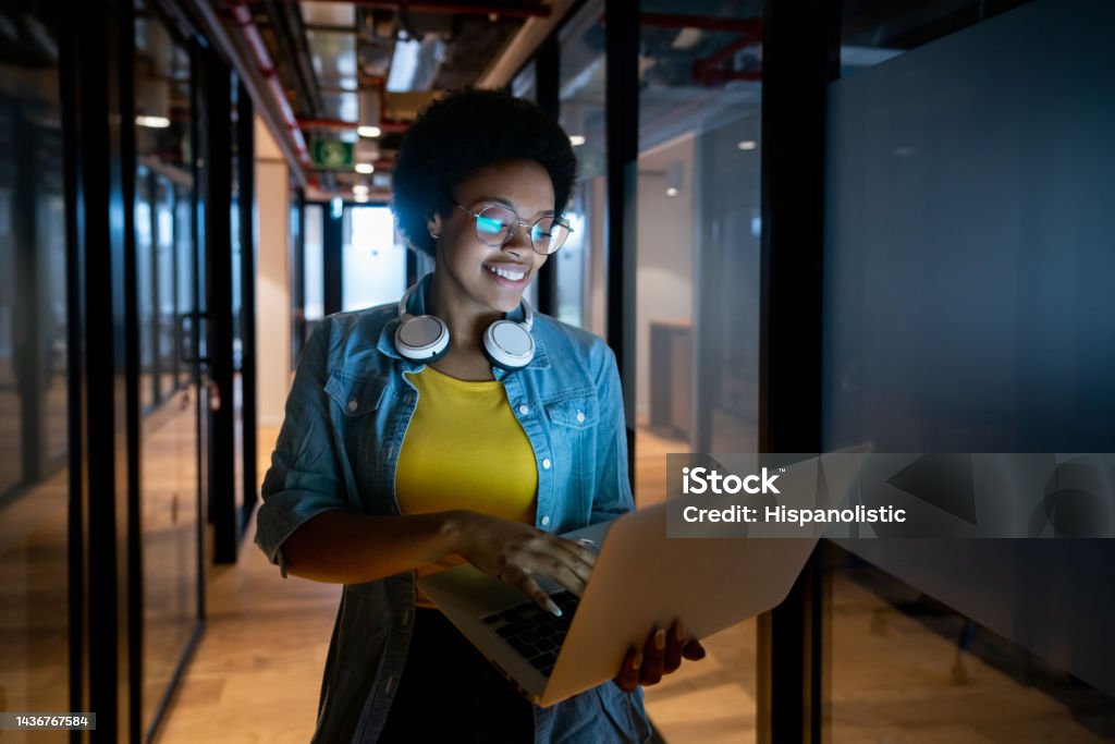 IT technician working late at the office using her laptop Portrait of an African American IT technician working late at the office using her laptop and smiling Data Scientist Stock Photo