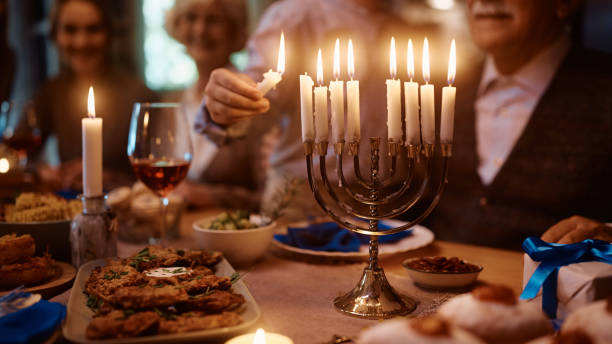 feche acima de menino acendendo velas em menorah enquanto celebrava hanukkah com sua família na mesa de jantar. - jewish tradition - fotografias e filmes do acervo