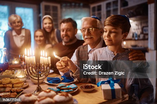 istock Happy Jewish boy and his grandfather lighting the menorah during family meal on Hanukkah. 1436771345