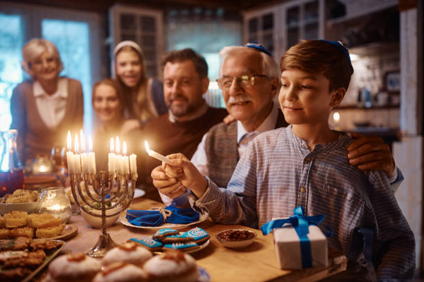 Happy Jewish boy and his grandfather lighting the menorah during family meal on Hanukkah. stock photo