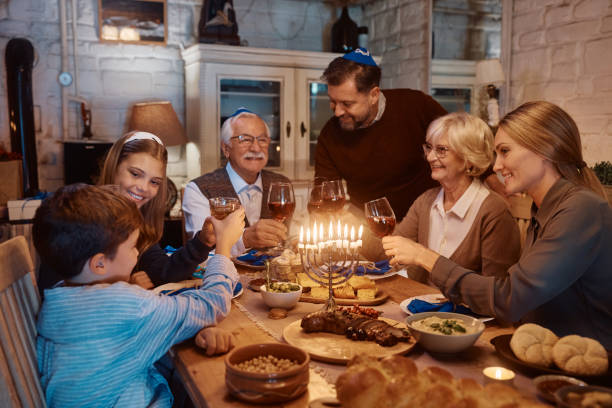 feliz brindis familiar de varias generaciones mientras se celebra hanukkah en la mesa del comedor. - los niños y los padres brindis bebidas mientras almuerza fotografías e imágenes de stock