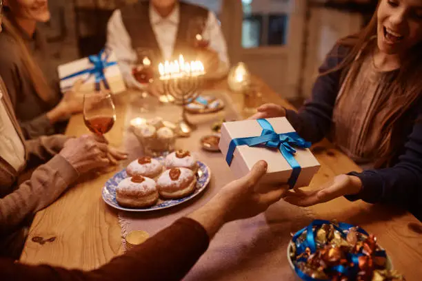 Close up of Jewish father giving his daughter gift box while celebrating Hanukkah with their family at home.