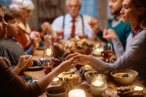 Close up of mother and daughter holding hands during family prayer on Thanksgiving. Close up of extended family saying grace during dinner at dining table on Thanksgiving. saying grace stock pictures, royalty-free photos & images