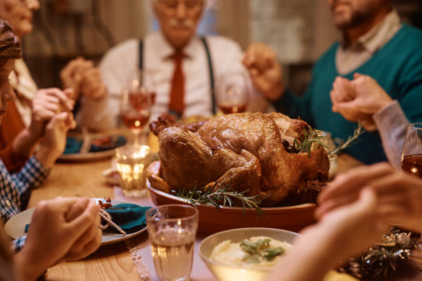 istock Thanksgiving turkey with family saying grace at dining table. 1436772955