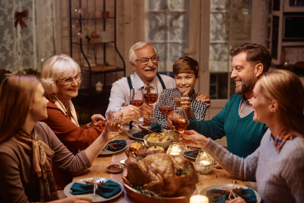 happy extended family toasting while celebrating thanksgiving at dining table. - family large american culture fun imagens e fotografias de stock